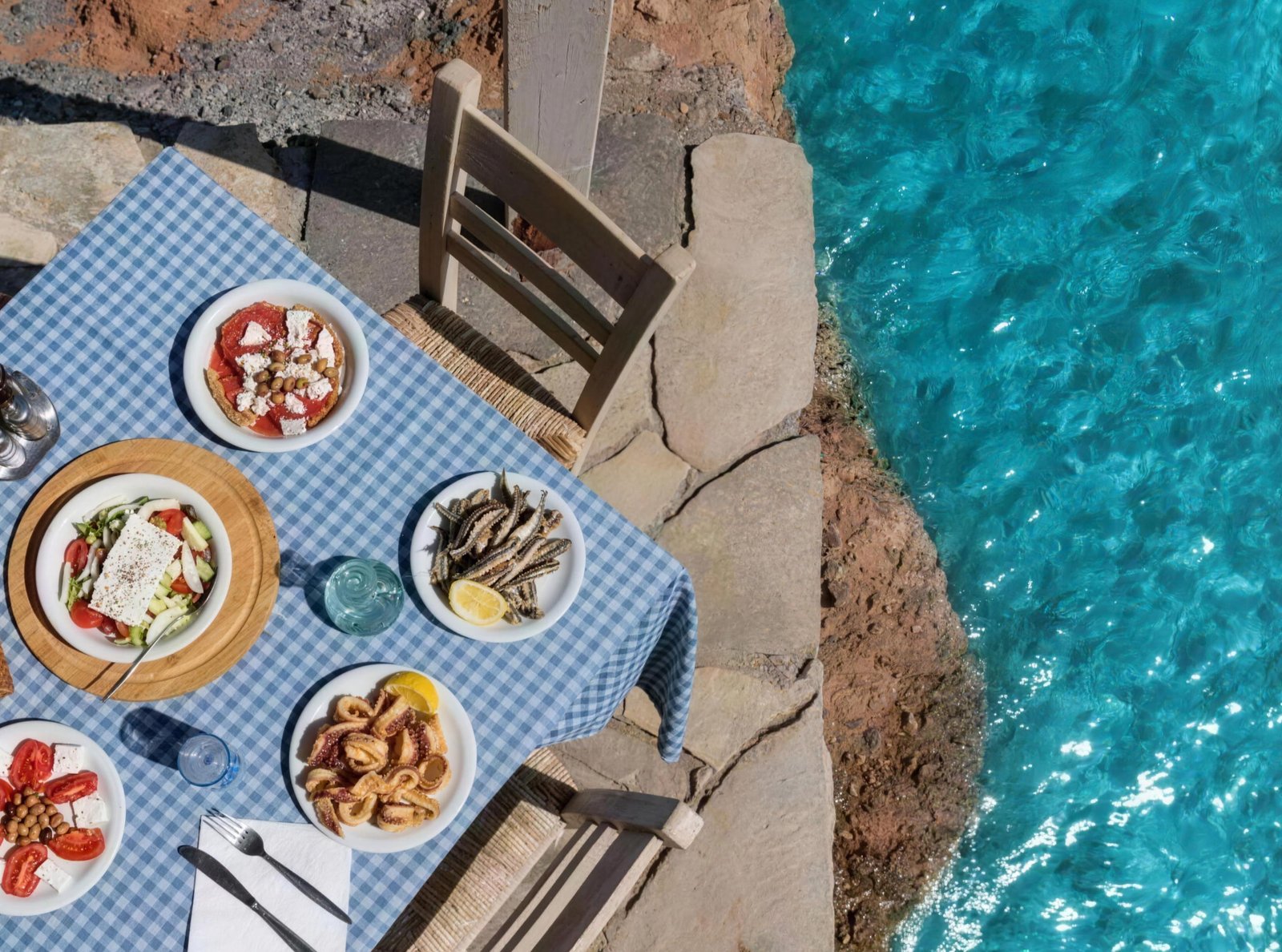 A Greek table of seafood, salad, and meze beside clear blue water