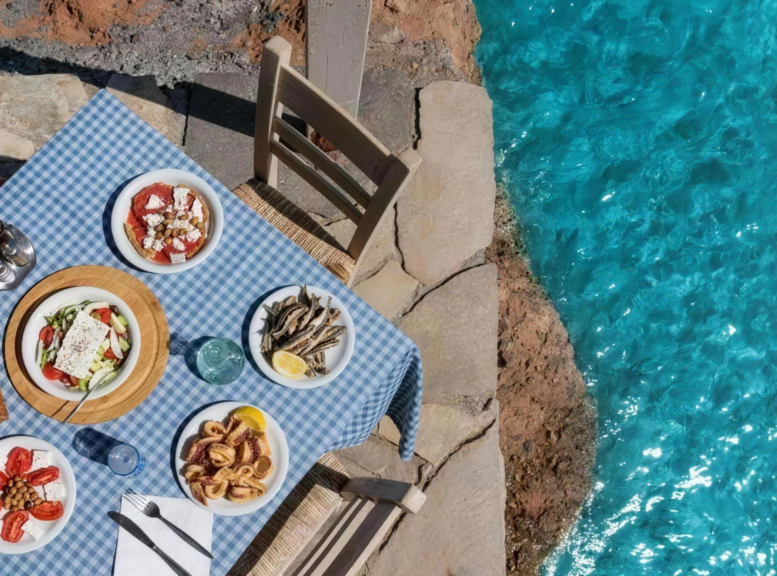 A Greek table of seafood, salad, and meze beside clear blue water